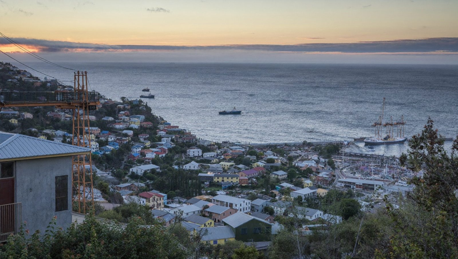 Una bahía al amanecer vista desde los cerros, con un puerto y barcos fondeados.